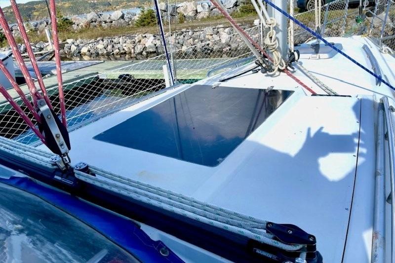 1990 CS 34 sailboat deck with ropes and hatch, docked near rocky shoreline.