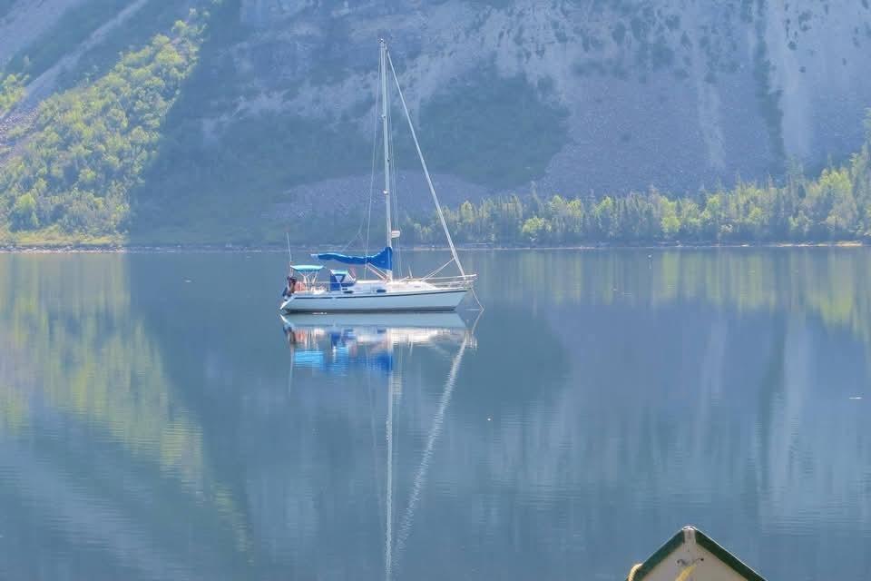 Sailboat on tranquil lake with mountain backdrop, CS 34 model, 1990.