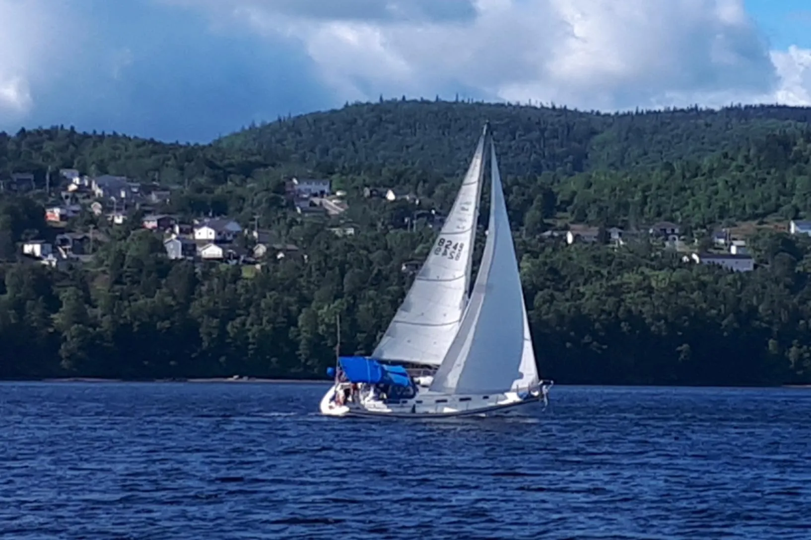 Sailboat CS 34 (1990) cruising on a lake with forested hills and houses in the background.