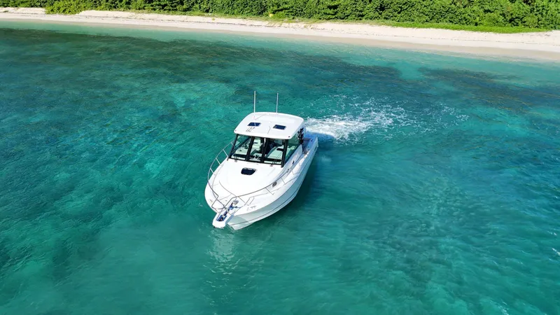  Yacht Photos Pics Boston Whaler 345 Conquest 2022 cruising in clear turquoise waters near a sandy beach.