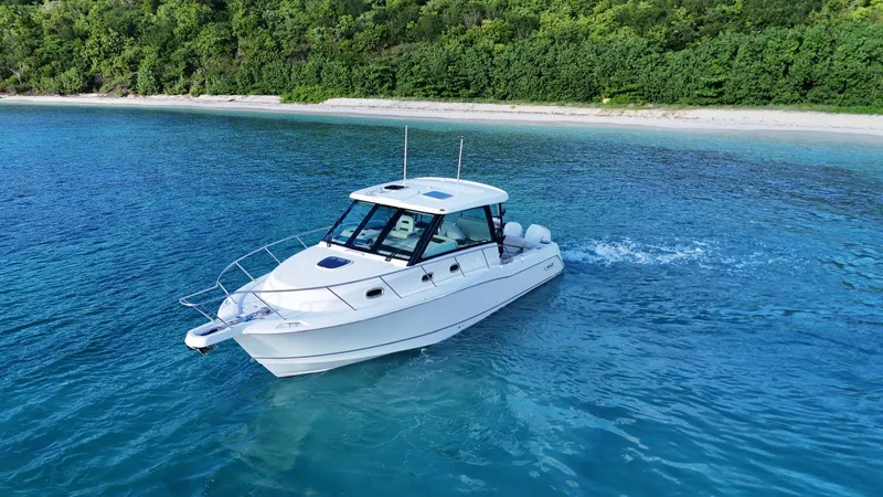  Yacht Photos Pics 2022 Boston Whaler 345 Conquest cruising in clear blue waters near a lush green shoreline.