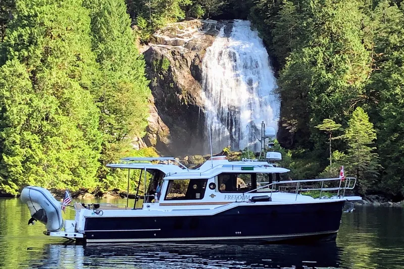  Yacht Photos Pics 2019 Ranger Tugs R-29 S boat near a scenic waterfall and lush forest.