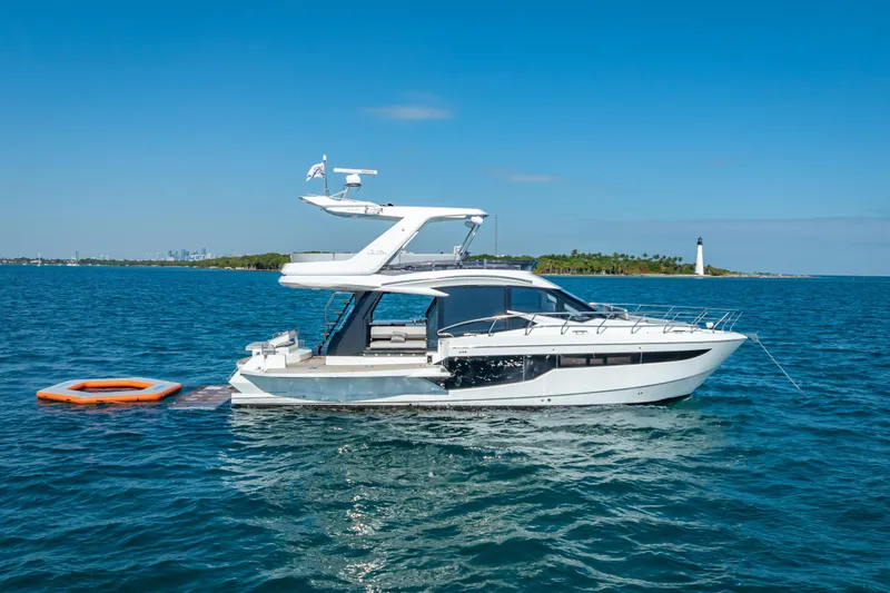  Yacht Photos Pics 2021 Galeon 500 Fly yacht anchored in serene blue waters near a lighthouse.