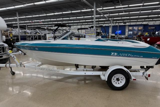 1991 Larson All American 170 boat on trailer in showroom, teal and white design.