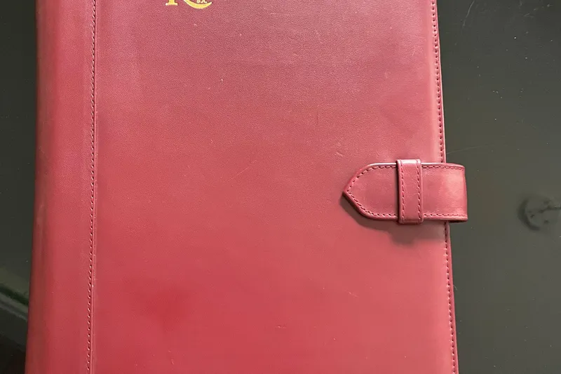 Spirit Yacht Photos Pics Red leather-bound book with a strap closure on a dark surface.