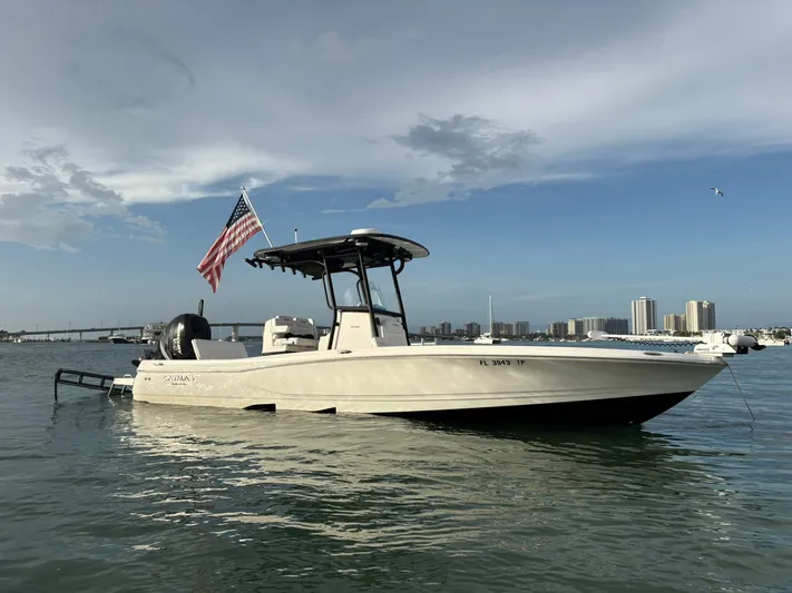  Yacht Photos Pics 2023 Caymas 28 HB boat on water with American flag, city skyline in background.