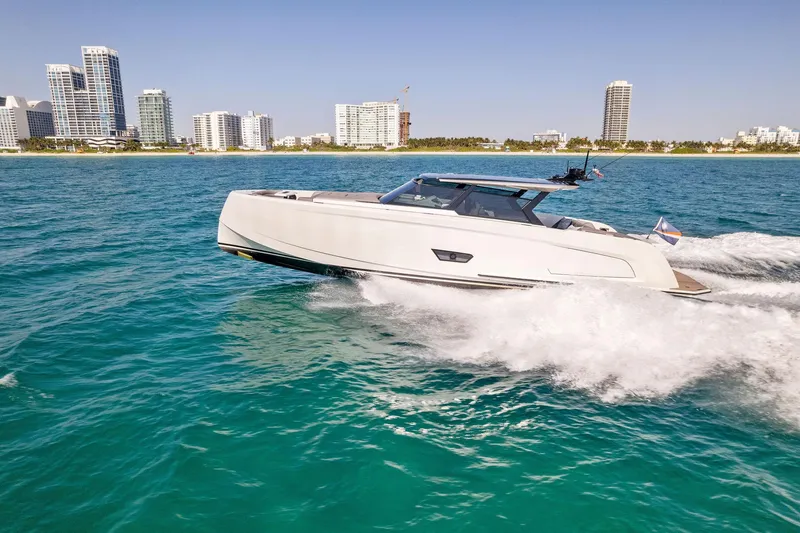 The Next Trade Yacht Photos Pics 2022 Vanquish Yachts VQ58 cruising on turquoise water near city skyline.