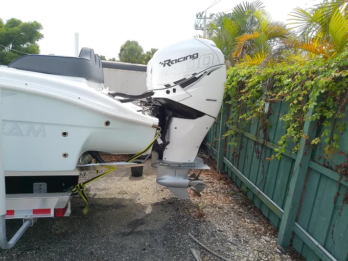  Yacht Photos Pics 2025 Glasstream 328 SCX boat with Mercury Racing outboard engine, parked near a green fence.
