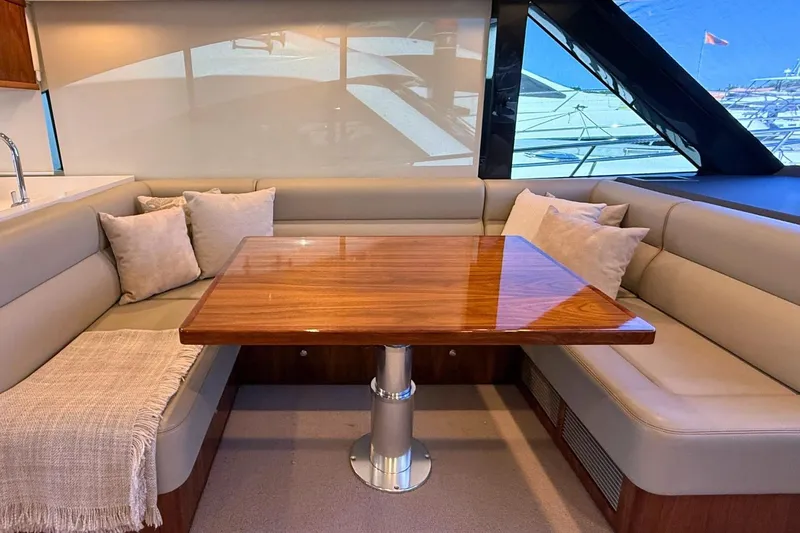 Buzz Yacht Photos Pics Luxurious interior of 2020 Riviera 57 Enclosed Flybridge with elegant wood table and plush seating.