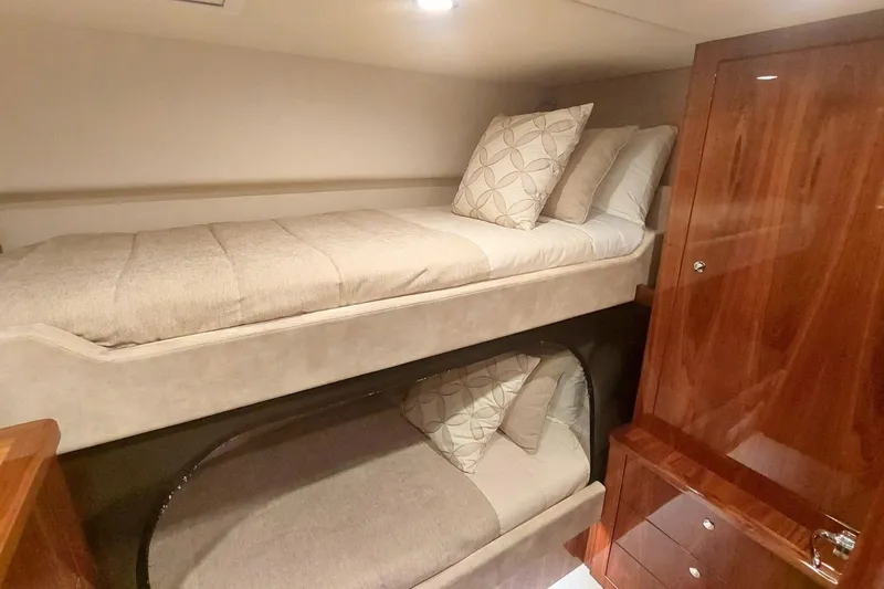 Buzz Yacht Photos Pics 2020 Riviera 57 Enclosed Flybridge cabin with cozy bunk beds and wooden cabinetry.