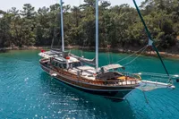 Aganlar Custom Motorsailer Gulet 2003 anchored in clear turquoise waters near a forested shoreline.