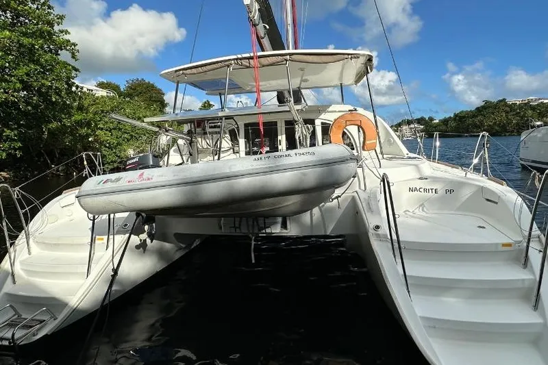 Nacrite Yacht Photos Pics 2018 Lagoon 380 catamaran docked, featuring a dinghy and lush greenery in the background.