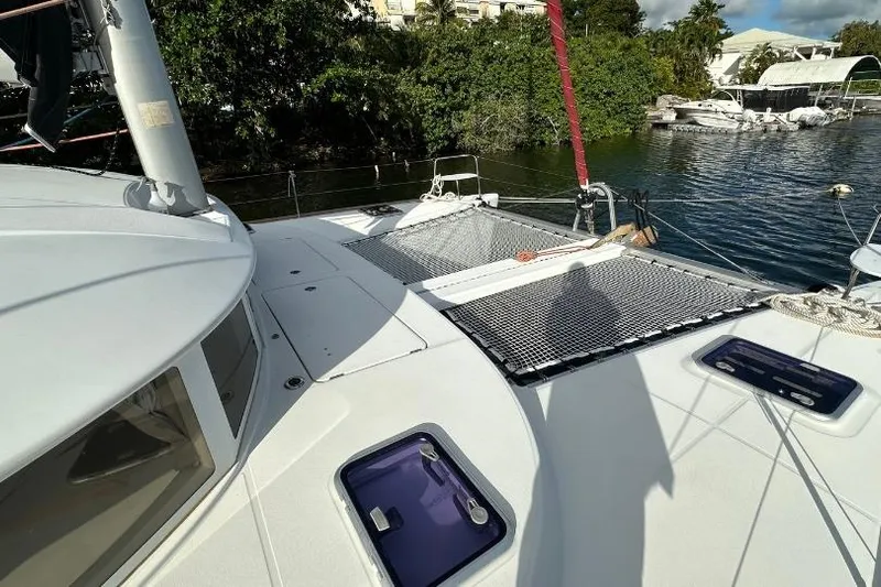 Nacrite Yacht Photos Pics 2018 Lagoon 380 catamaran deck with netting, docked near lush greenery.