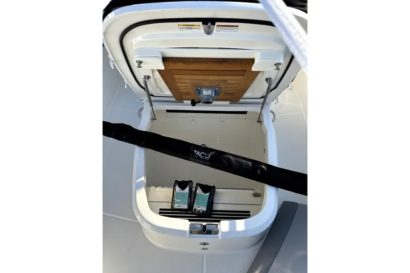  Yacht Photos Pics Open storage compartment on 2023 Boston Whaler OUTRAGE boat, featuring wooden panel and accessories.