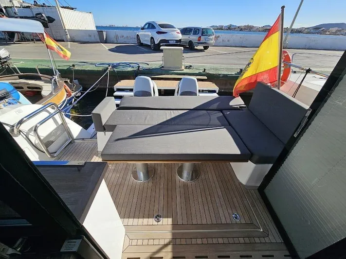  Yacht Photos Pics 2024 Sealine C390V yacht deck with seating, Spanish flag, and docked boats in the background.