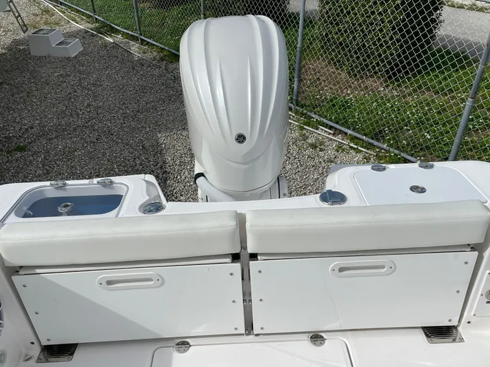 White Yacht Photos Pics 2023 Everglades 235CC boat with white seating and engine, parked near a chain-link fence.