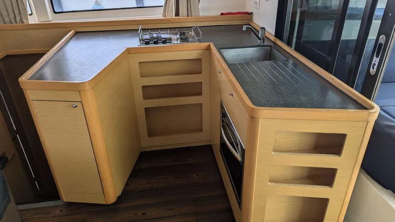 Mango IV Yacht Photos Pics Compact kitchen area in a 2017 Lagoon 42 yacht with stove, sink, and wooden cabinetry.