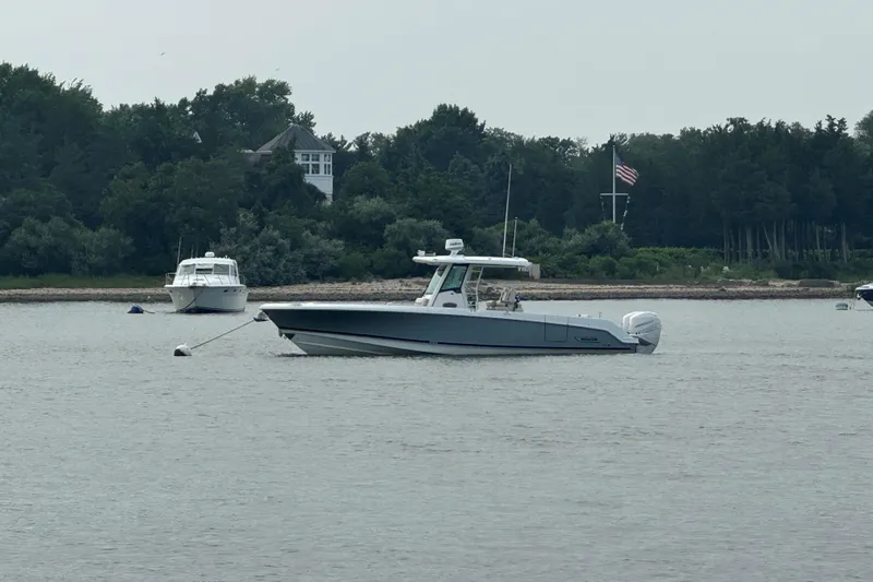  Yacht Photos Pics 2018 Boston Whaler 330 Outrage boat anchored on calm water near a wooded shoreline.