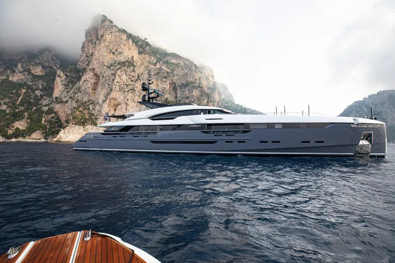 Utopia IV Yacht Photos Pics Luxurious 2018 Rossinavi Custom yacht near rocky coastline under cloudy sky.