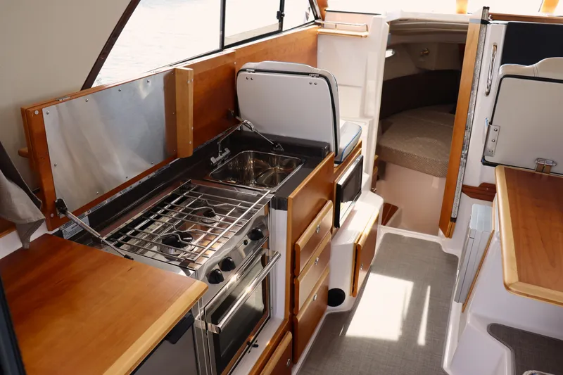 The Islander Yacht Photos Pics 2018 Cutwater C-302 Coupe interior with kitchen, stove, and seating area.