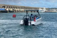 2022 Axopar 22 T-Top boat cruising near a coastal pier under a cloudy sky.