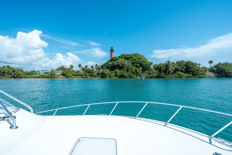 Big Hit Yacht Photos Pics Cabo 40 Express 2020 yacht cruising near lush island with lighthouse under blue sky.