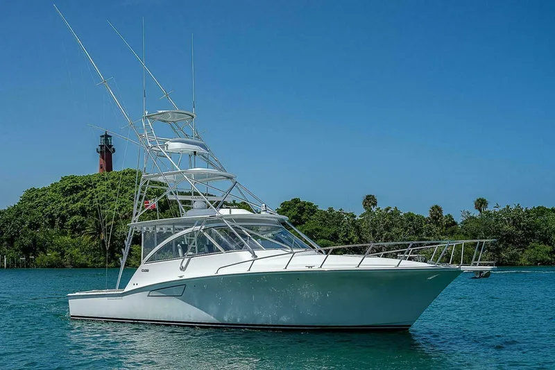 Big Hit Yacht Photos Pics 2020 Cabo 40 Express yacht on clear blue water near lush greenery and lighthouse.