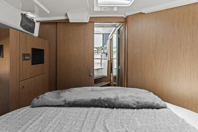 Trinity Yacht Photos Pics 2020 Jeanneau NC 1095 Fly cabin interior with bed, wooden walls, and open door.