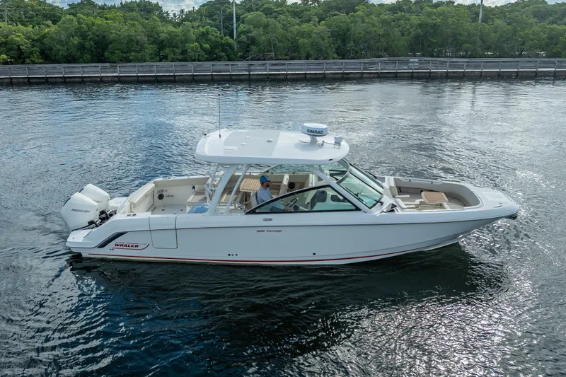 Trade In-- Bring All Offers & Trades Yacht Photos Pics 2024 Boston Whaler 320 Vantage boat cruising on calm water near a wooded shoreline.