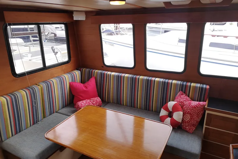  Yacht Photos Pics Cozy Nordic Tug 32 interior with striped seating, wooden table, and colorful cushions, 1990 model.