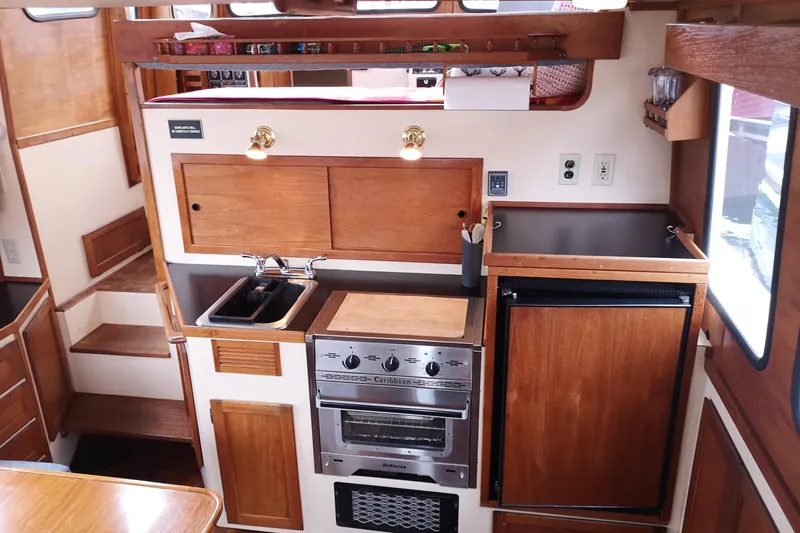  Yacht Photos Pics Cozy 1990 Nordic Tug 32 galley with wood cabinetry, stove, sink, and compact fridge.