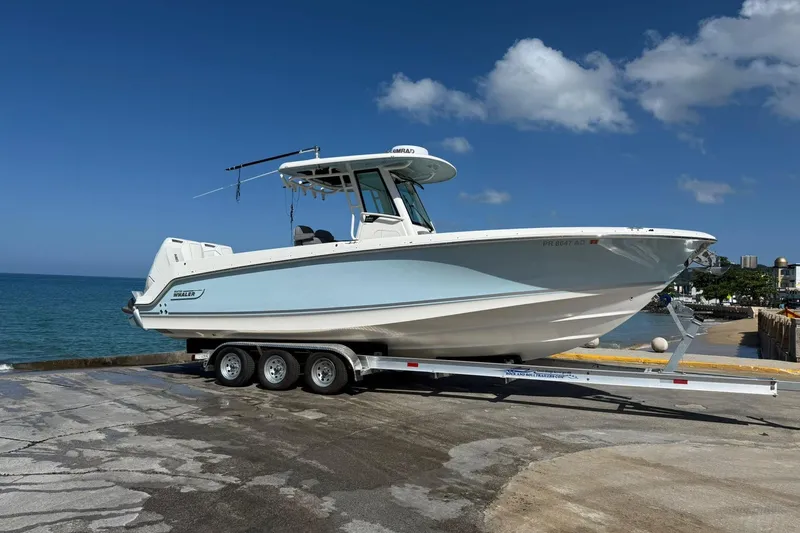  Yacht Photos Pics 2024 Boston Whaler 280 Outrage boat on trailer by the ocean under a clear blue sky.