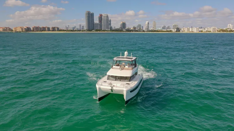 Hawkeye Yacht Photos Pics 2022 Fountaine Pajot MY6 yacht cruising in turquoise waters with city skyline backdrop.