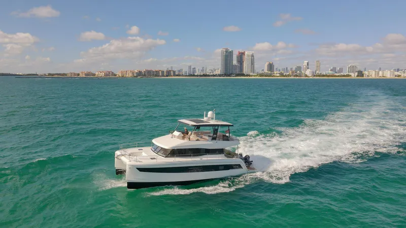 Hawkeye Yacht Photos Pics 2022 Fountaine Pajot MY6 yacht cruising on turquoise waters near a city skyline.