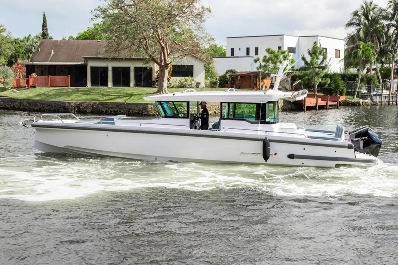  Yacht Photos Pics 2024 Axopar 37XC CROSS CABIN cruising on a scenic waterway near modern homes.