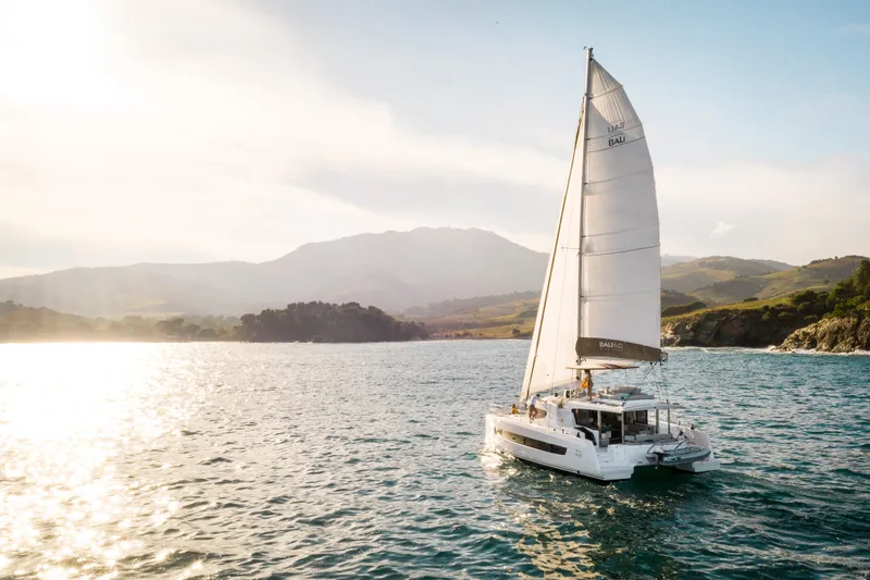  Yacht Photos Pics Sailing catamaran Bali 4.6 (2026) on serene waters with scenic mountain backdrop.