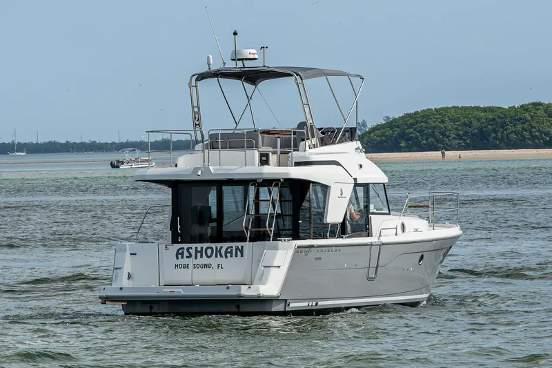Ashokan Yacht Photos Pics 2022 Beneteau Swift Trawler 35 cruising on calm waters near a sandy shoreline.