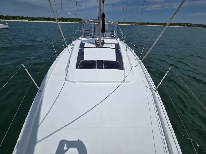 Off-piste Yacht Photos Pics 2019 Beneteau Oceanis 46.1 sailboat on calm water, clear sky, and distant shoreline.