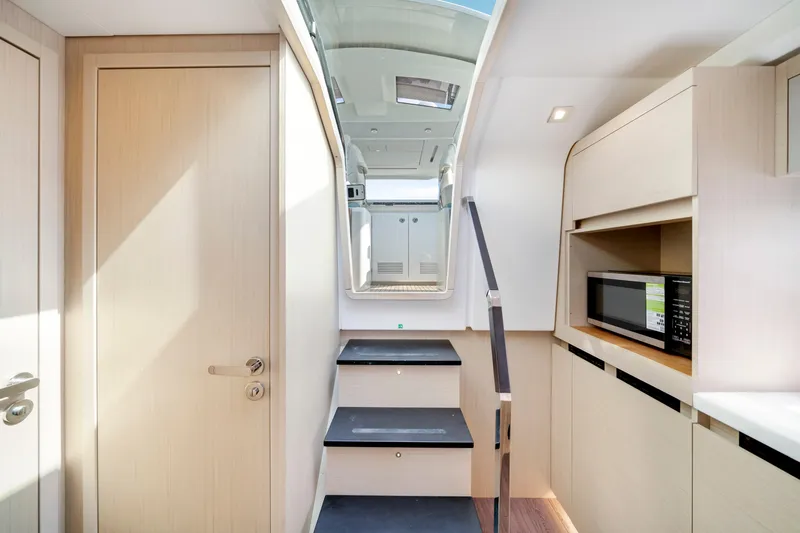  Yacht Photos Pics 2024 Jeanneau DB/43 OB interior with modern cabinetry, stairs, and built-in microwave.