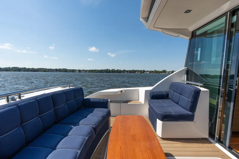 Pyrite Yacht Photos Pics 2015 Tiara Yachts C44 Coupe deck with blue seating and wooden table, overlooking water.