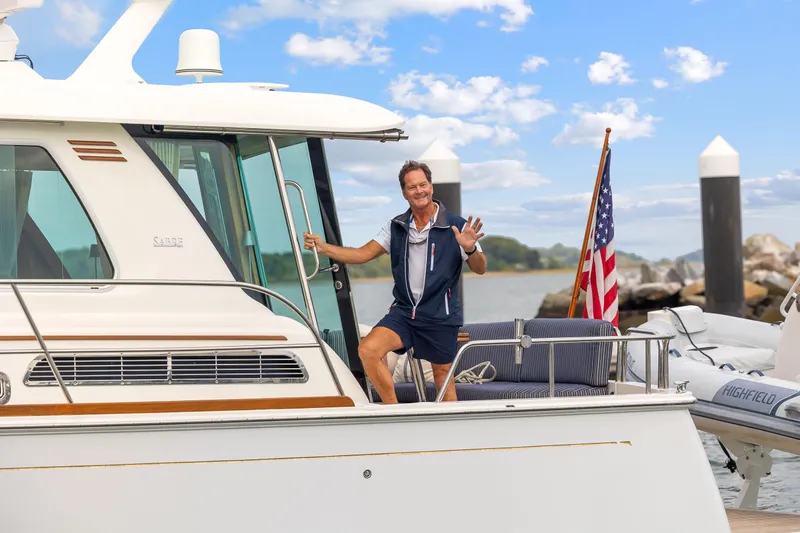 Second Rodeo Yacht Photos Pics Man waving on 2018 Sabre 48 Salon Express yacht, docked with American flag.