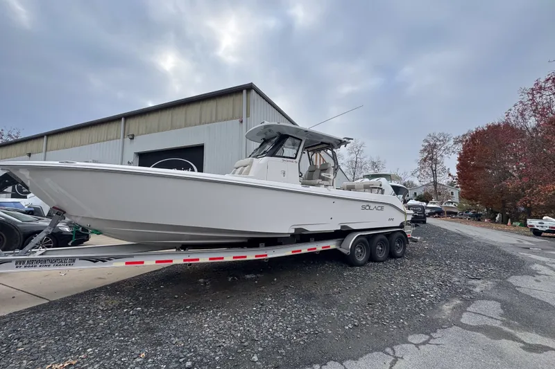  Yacht Photos Pics 2025 Solace 30 HCS boat on trailer outside a warehouse, under cloudy sky.