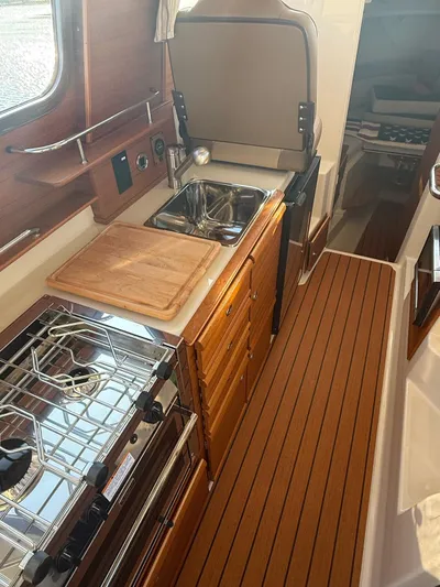 Yacht Photos Pics 2023 Ranger Tugs R-27 interior kitchen with stove, sink, and wooden cabinetry.
