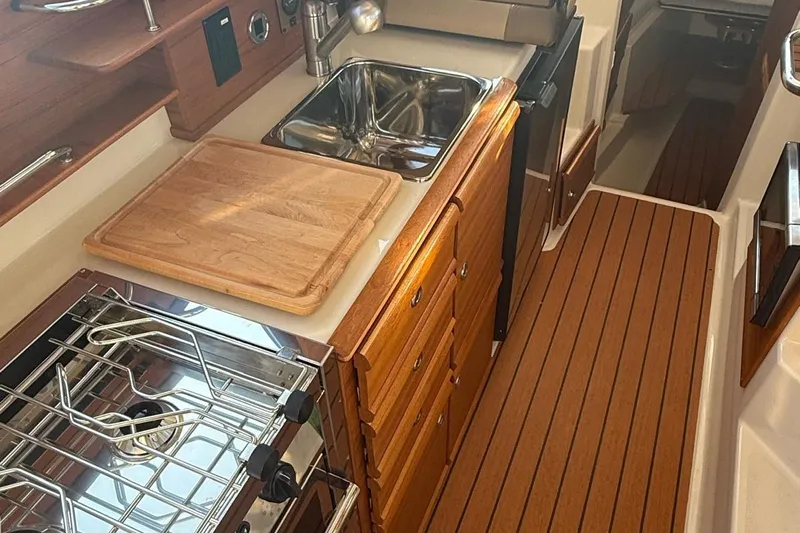  Yacht Photos Pics 2023 Ranger Tugs R-27 galley with stove, sink, and wooden cabinetry.