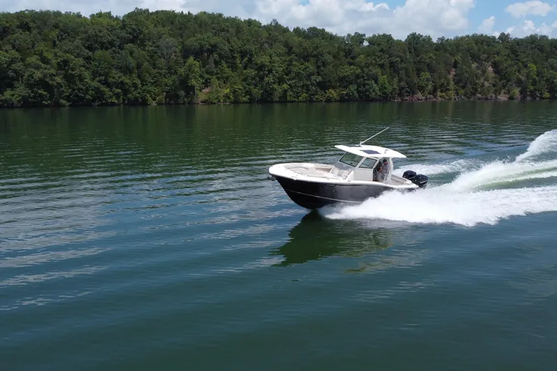  Yacht Photos Pics 2021 Scout 330 LXF boat cruising on a serene lake with lush forest backdrop.