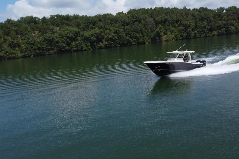  Yacht Photos Pics 2021 Scout 330 LXF boat cruising on a serene lake with lush green forest backdrop.