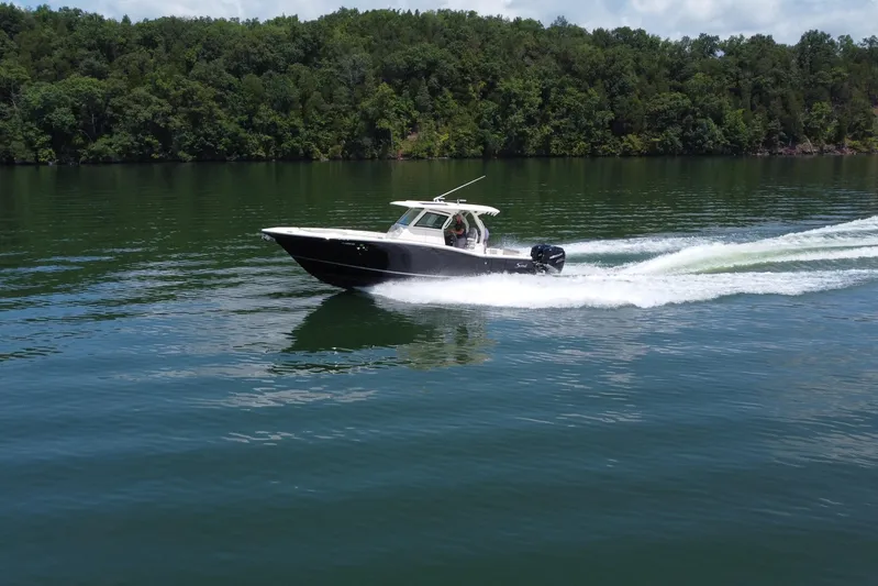 Yacht Photos Pics 2021 Scout 330 LXF boat cruising on a serene lake with lush green forest backdrop.