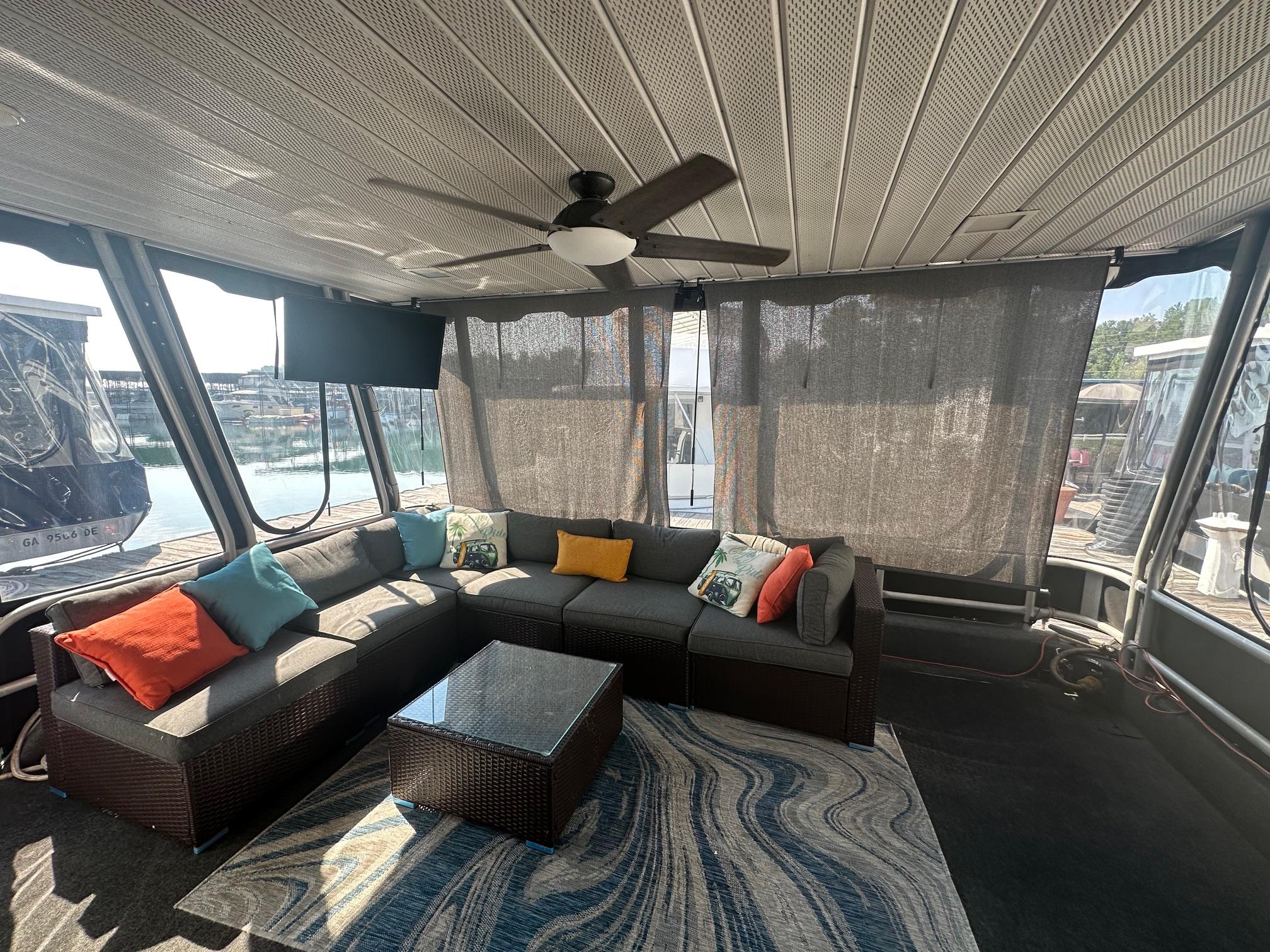 Houseboat interior with wicker furniture, colorful cushions, and a ceiling fan, Lakeview 15x70, 1995 model.