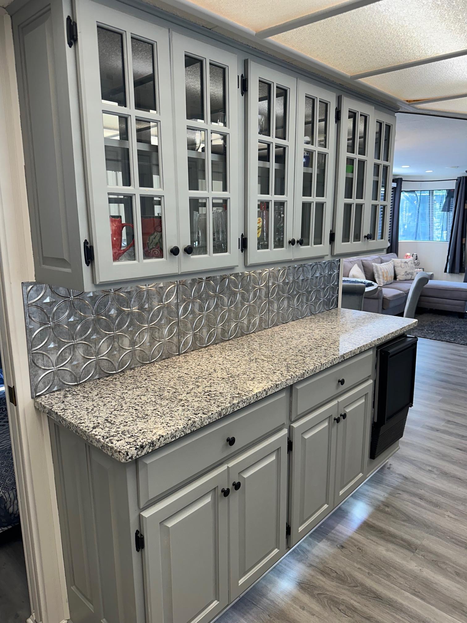Gray kitchen cabinets with glass doors, granite countertop, and decorative backsplash in a Lakeview 15x70 model.