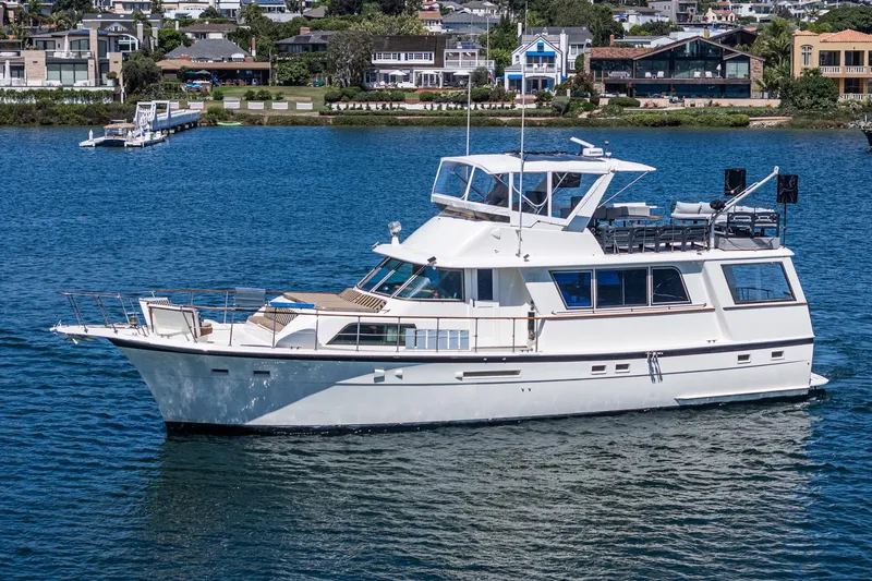 Maverick Yacht Photos Pics 1979 Hatteras 58 Motor Yacht cruising on a serene blue lake near waterfront homes.
